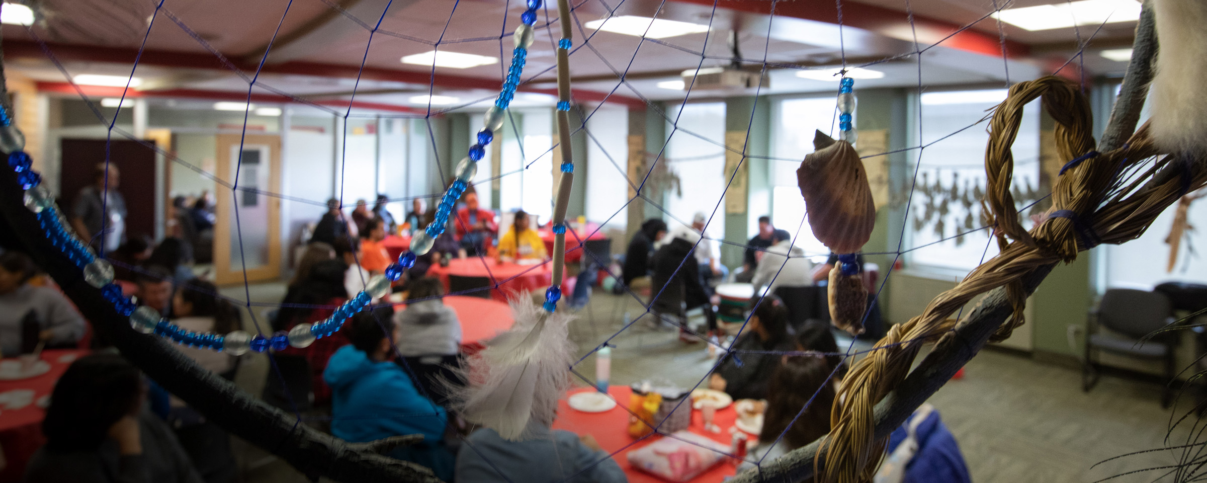 Gathering space with people seated at tables, as seen through close-up of an Indigenous dreamcatcher.