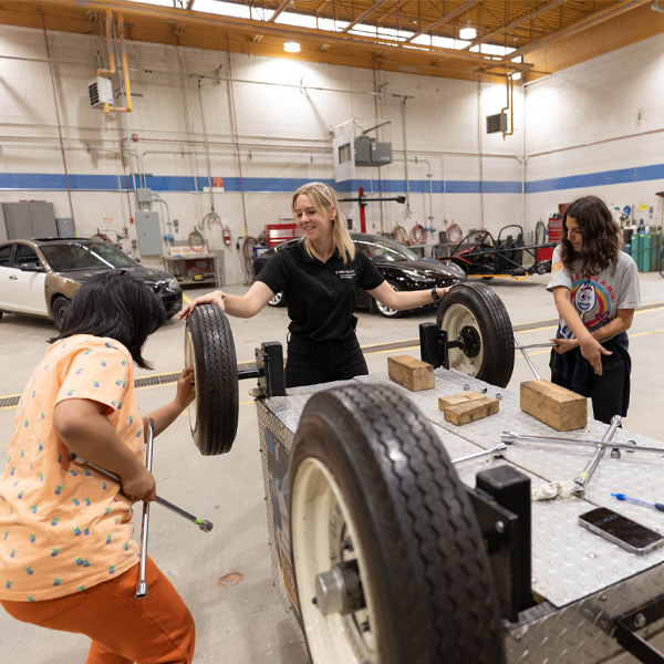two girls with teacher working on a car